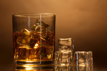 glass of whiskey and ice on brown background