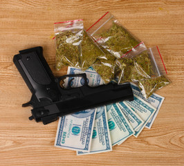 marihuana in packages, dollars and handgun on wooden background