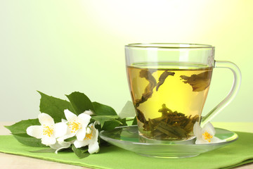 cup of green tea with jasmine on table on green background