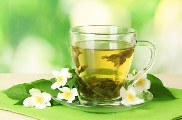 cup of green tea with jasmine on table on green background