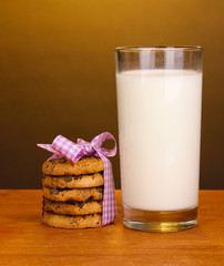 Glass of milk and cookies on wooden table on brown background