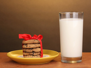 Glass of milk and cookies on wooden table on brown background