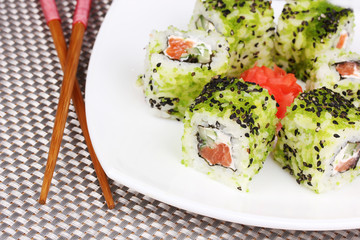 Tasty rolls on plate with chopsticks on grey mat close-up