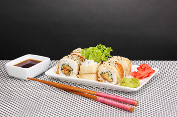 Tasty rolls on plate with chopsticks on mat on grey background