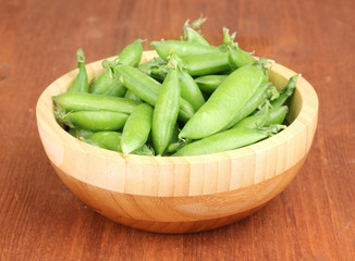 Green peas in wooden bowl on wooden background