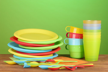 bright plastic tableware on wooden table on colorful background