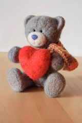Серый мишка-игрушка держит красное сердце