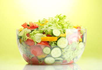 fresh vegetable salad in transparent bowl on green background