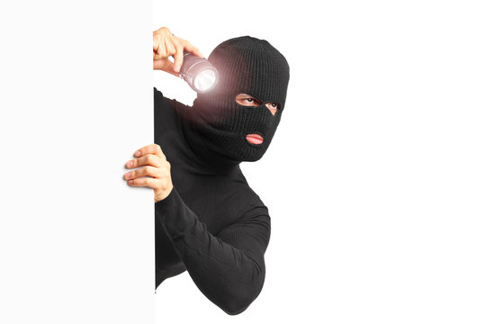 A thief with robbery mask holding a flashlight behind a white pa