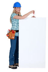 Tradeswoman holding a screwdriver over a blank sign
