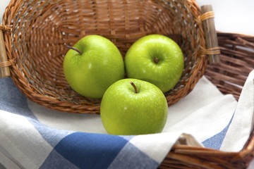 Three green apples in the brown wicker basket