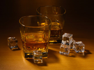 two glasses of scotch whiskey and ice on wooden table