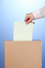 Hand with voting ballot and box on blue background