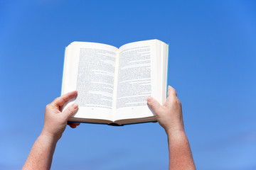 Hände halten ein Buch gegen den blauen Himmel