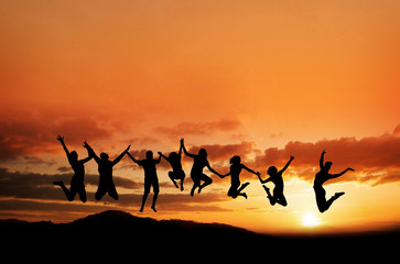 silhouette of teenagers jumping in sunset on mountain range