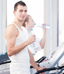 Man and woman drinking water after sports in gym