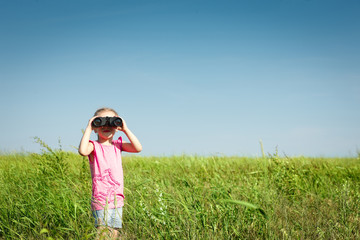 Little girl in field looking away through binoculars at you