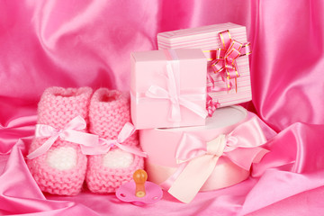 pink baby boots, pacifier, gifts on silk background.