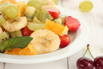 Fresh fruits salad on plate and berries on white wooden table