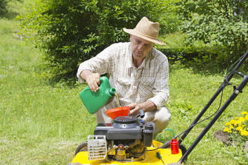 Mid age man adding oil to lawn mover in the garden