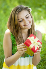 Beautiful teen girl with gift in the park at green grass.