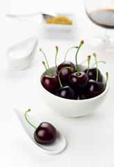 Cherries on white spoon and bowl, sherry glass, sugar cane