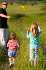 Fototapeta premium Father and his children play with frisbee on sunny spring day