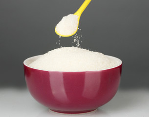 A colorful bowl full of white sugar with bright spoon
