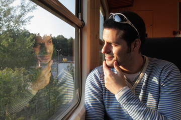 Mann betrachtet sein Spiegelbild im Zugabteil