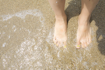 波打ち際に立つ女性の足