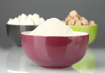 Bowls with different types of sugar on a gray background