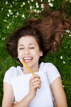 Girl lying on grass with workbook and pencil