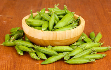 Green peas in wooden bowl on wooden background