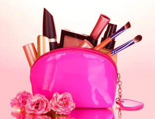Make up bag with cosmetics and brushes on pink background