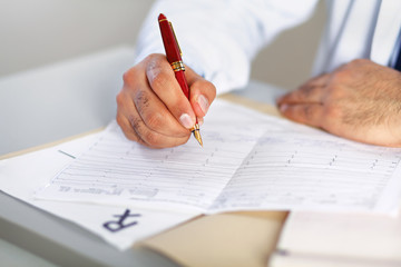 Hands of a doctor filling RX prescription, documents at the desk
