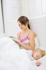 Obraz na płótnie Canvas Mother in bedroom reading book while baby sleeping