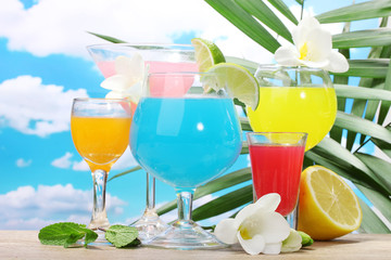 exotic cocktails and flowers on table on blue sky background
