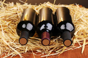 Bottles of great wine on hay on wooden table