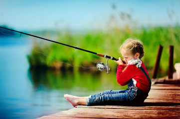 little girl fishing from wooden dock on lake