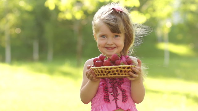 Child holding basket of strawberries and looking at camera