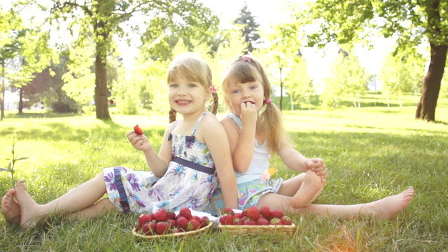 Happy girls eating strawberries. Sitting on the grass. Dolly HD