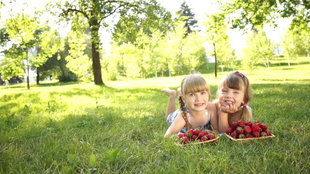 Laughing girls lying on the grass near strawberries