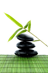 Fototapeta na wymiar black zen pebbles and a bamboo leaf on green mat