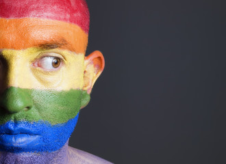 Gay flag painted on the face of a man. Man is looking sideways