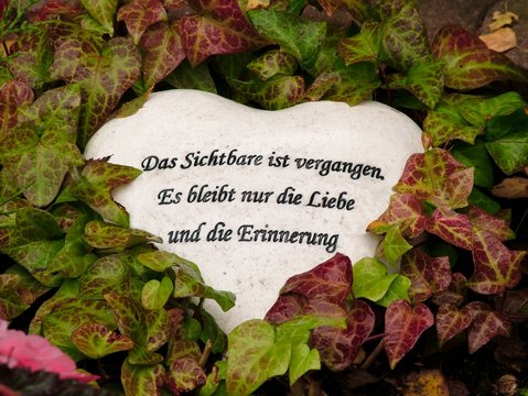 Das Sichtbare ist vergangen, es bleibt nur die Liebe und die Erinnerung, Inschrift auf einem Herz aus Stein zwischen Efeu, Gedenken