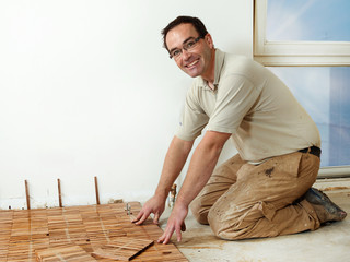 Smiling carpenter at work is fitting wood parquet on the floor