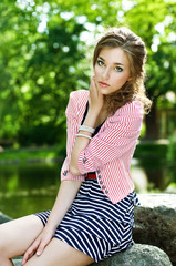 Fototapeta premium pretty young girl sitting on stones next to the pond