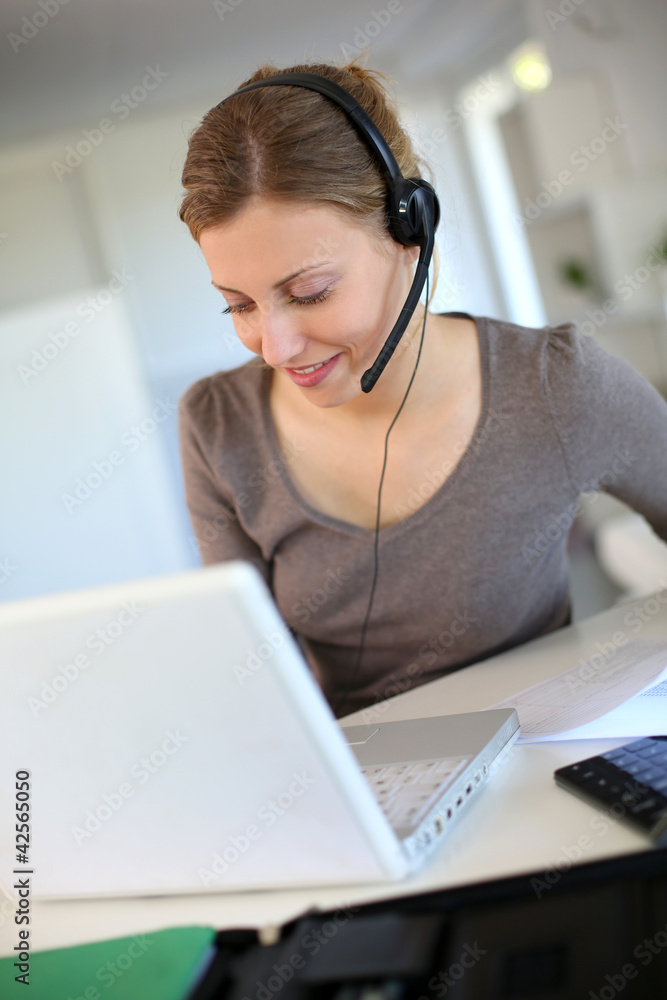 Wall mural Young woman working from home with laptop and headset