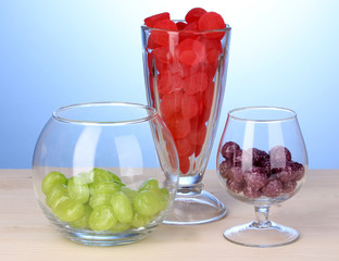 Color candies in glasses on wooden table on blue background