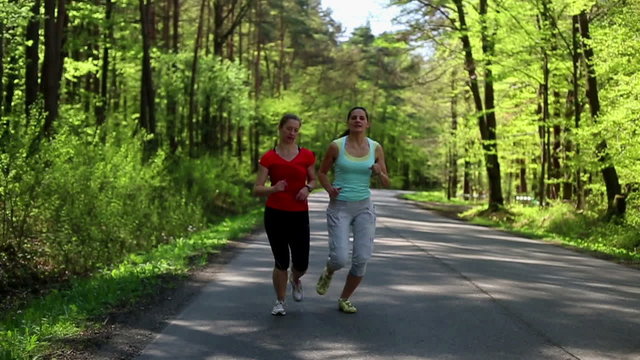 Two happy woman jogging in the forest, steadycam, slow motion